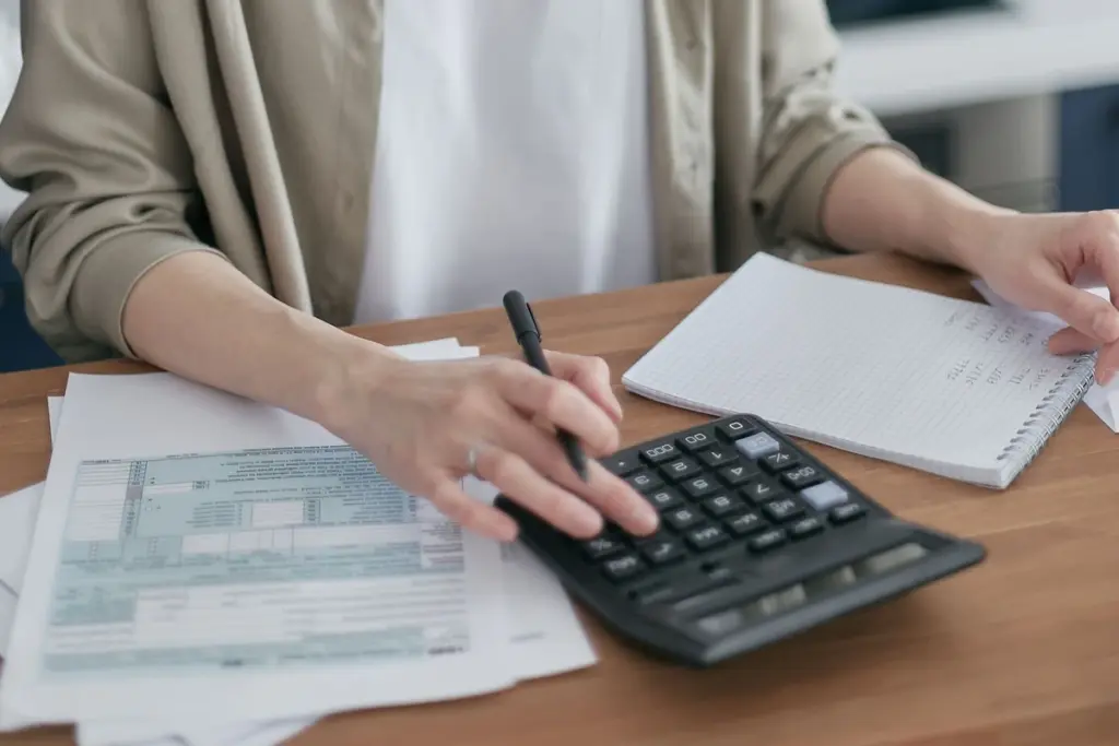 Manos haciendo cuentas con una calculadora, un cuaderno y unos papeles