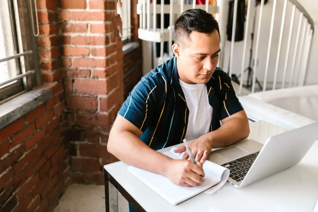 Persona estudiando en casa con un portátil y una libreta